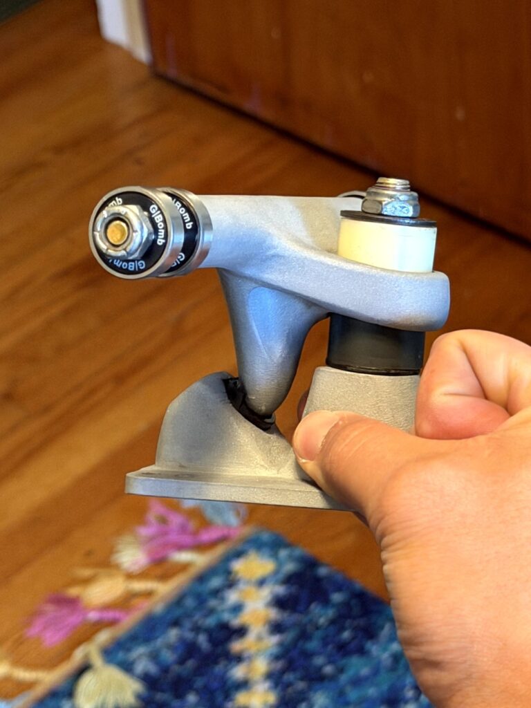 Side view of a metal 3D-printed Pantheon surf skate truck prototype showing the forward pivot and bushing stack